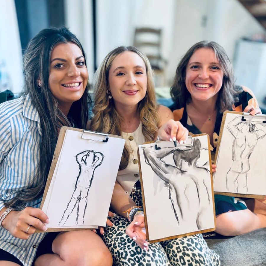 Bride and friends showing off their life drawings with beaming smiles wearing pink and black berets.