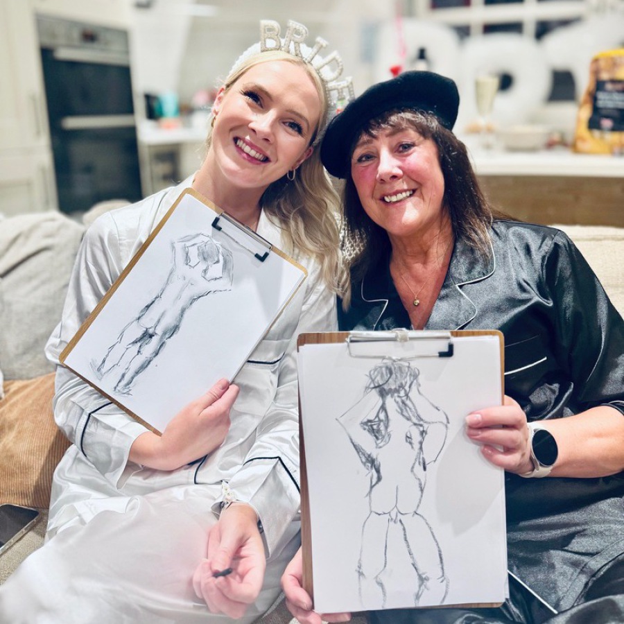 Bride and friend holding nude life drawings after mobile hen party life drawing session.