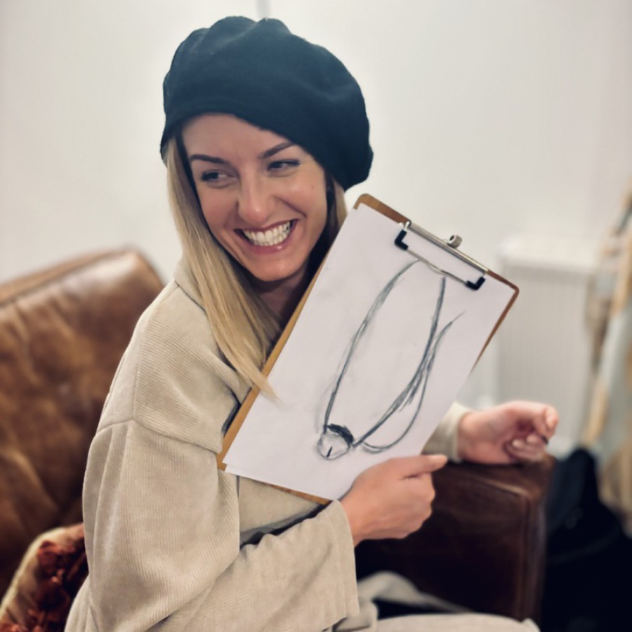 Woman wearing a black beret and beige jacket, holding a clipboard with a playful charcoal sketch from an award-winning life drawing hen party by Artful Hen Parties.