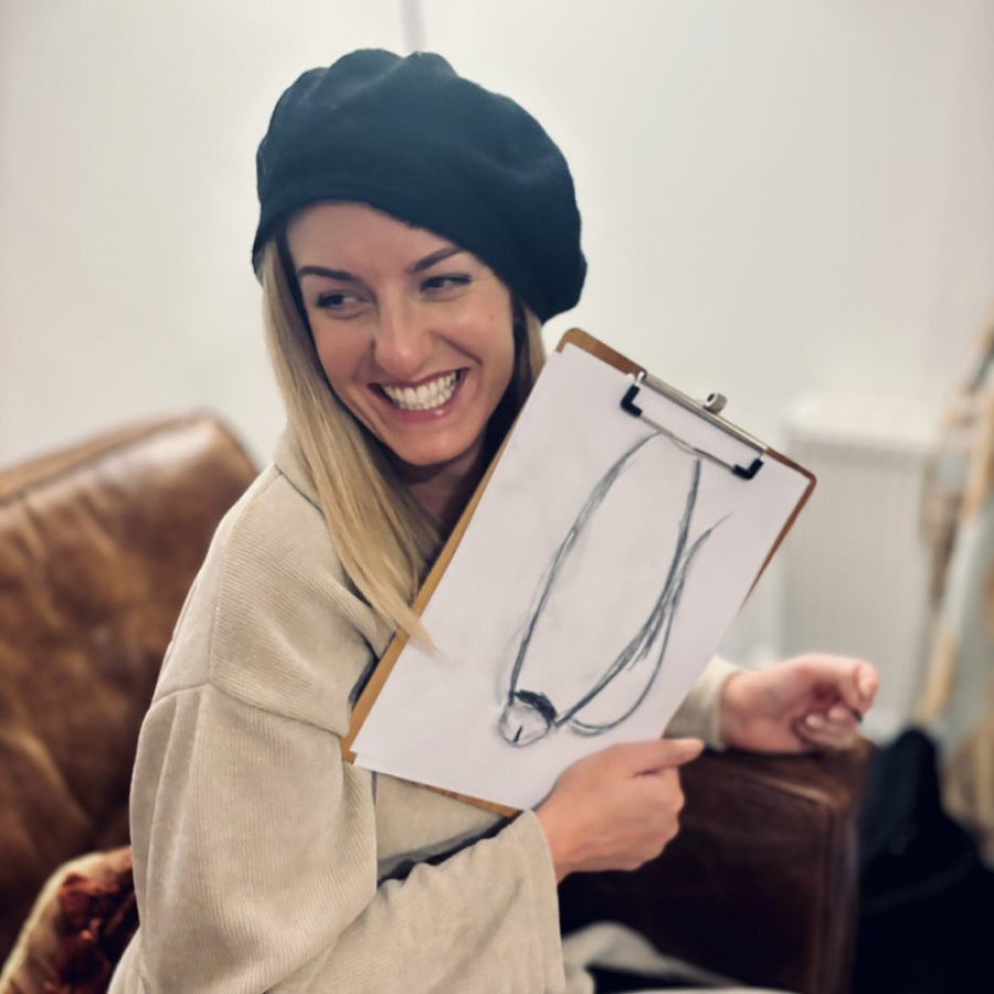 Woman wearing a black beret and beige jacket, holding a clipboard with a playful charcoal sketch from an award-winning life drawing hen party by Artful Hen Parties.